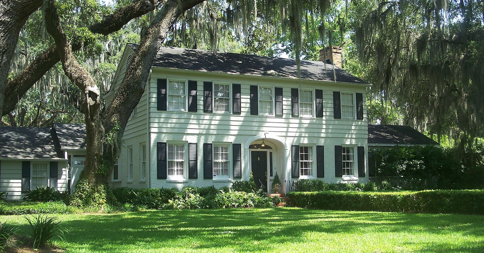A white two-story house with black shutters under live oaks and Spanish moss in Old Ortega, Jacksonville