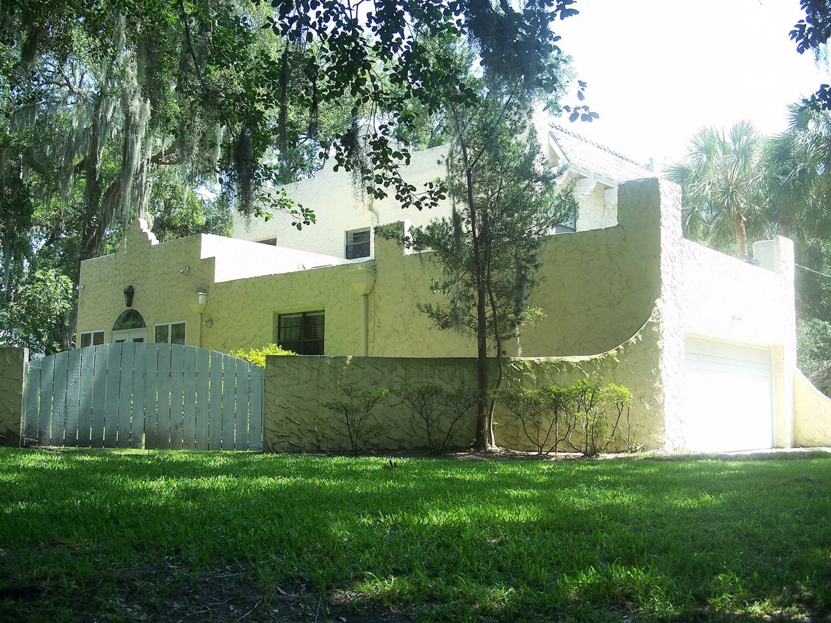 A stucco house with a wooden gate and a green lawn under oaks in Old Ortega, Jacksonville